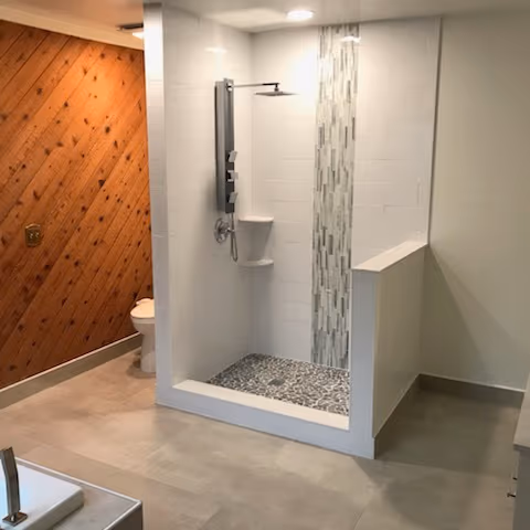 New tiled shower with a glass mosaic accent column and pebble floor