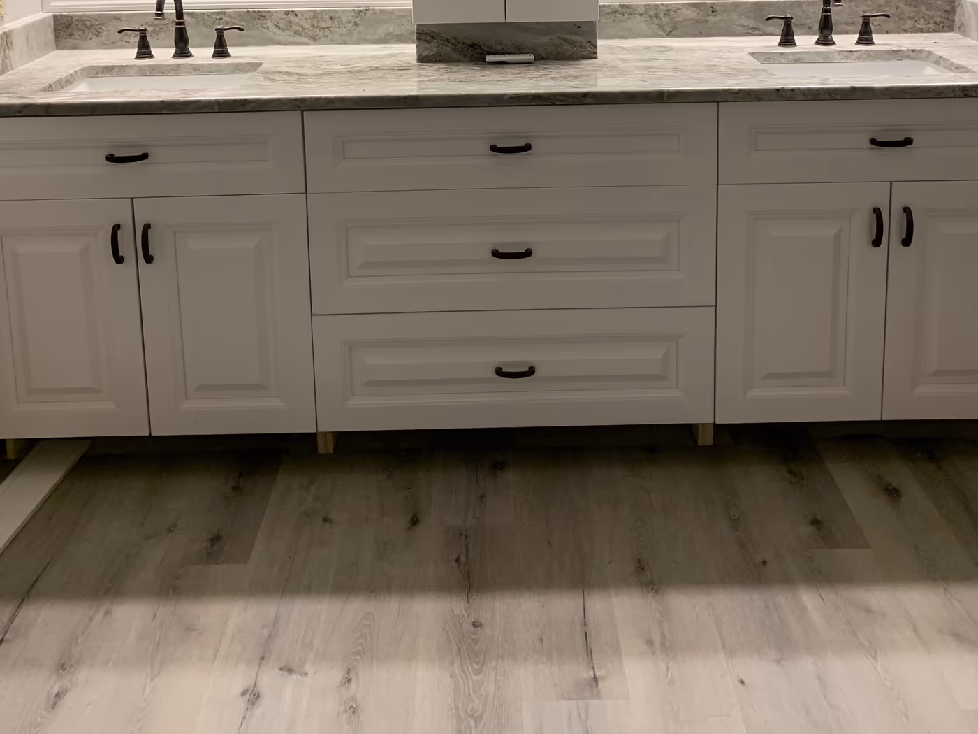 Same vanity wall rebuilt with white cabinets, stone counters, bronze faucets, and new plank flooring