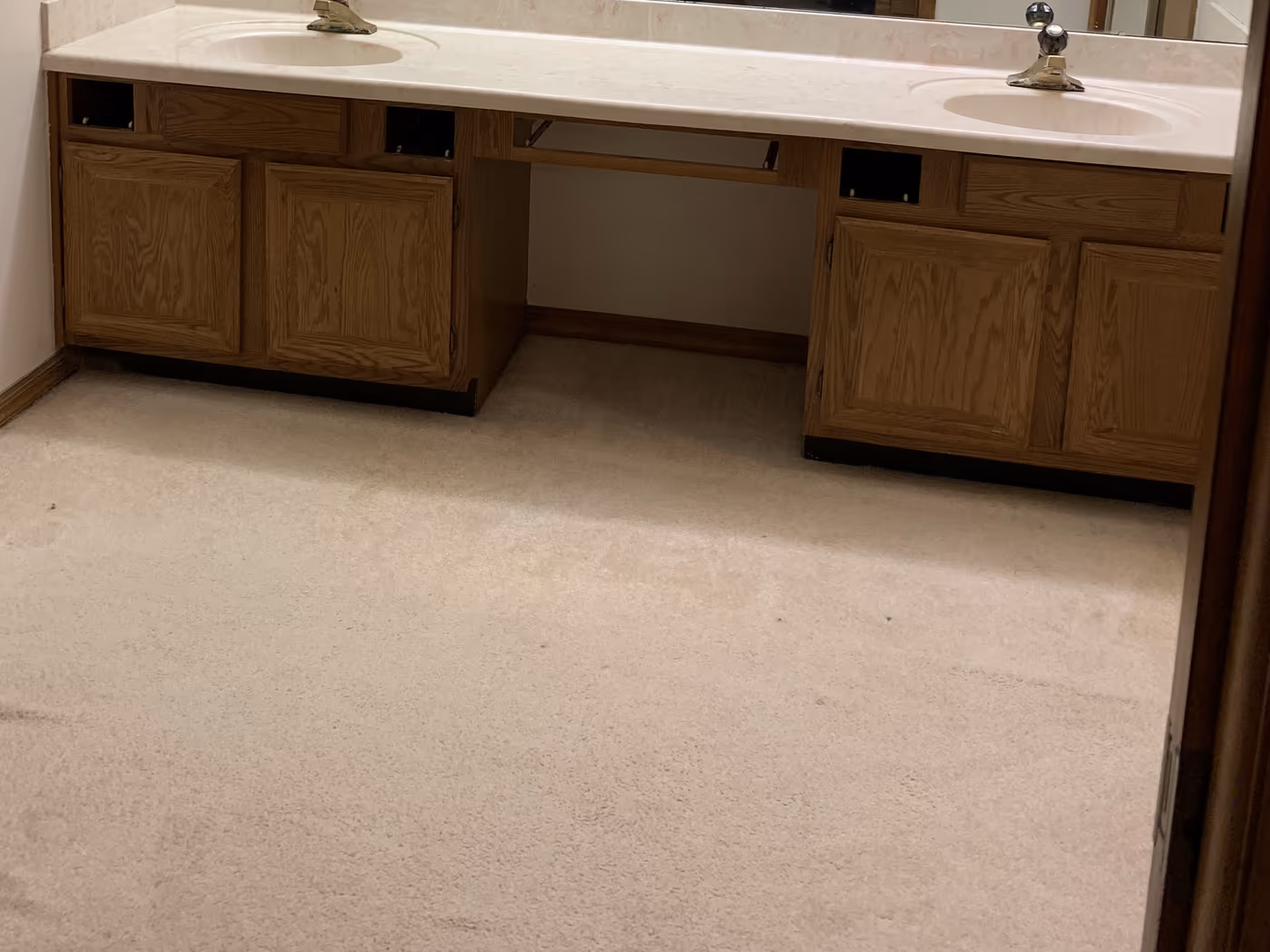 Dated oak double vanity with a cultured marble top and carpeted bathroom floor before the remodel