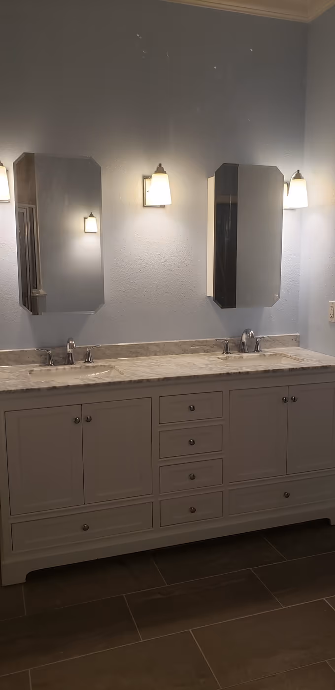 Remodeled bathroom with a white double vanity, stone counter, and new lighting